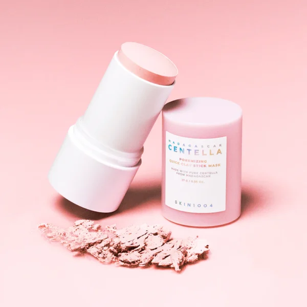 Madagascar Centella Poremizing Quick Clay Stick Mask ouvert, montrant la texture solide du masque et de la poudre d'argile étalée à côté, sur un fond rose pastel.