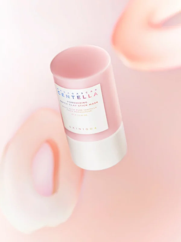 Madagascar Centella Poremizing Quick Clay Stick Mask en lévitation sur fond rose flou, mettant en valeur le design doux et élégant du stick.